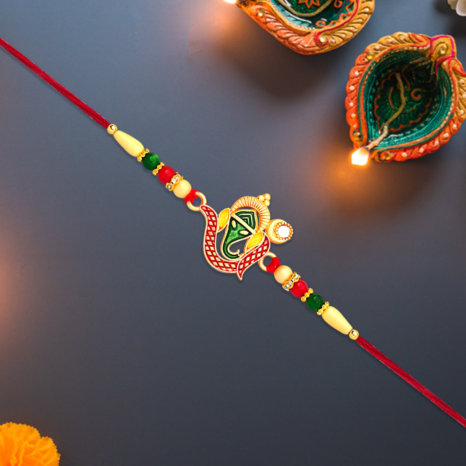 Green Enamel Lord Ganesha Rakhi With Decorative Red Thread And Golden Accents Green Enamel Lord Ganesha Rakhi With Decorative Red Thread And Golden Accents
